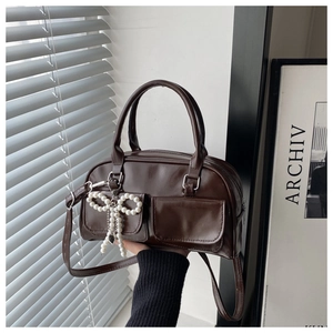 Detail of dark coffee shoulder bag with twin front pockets and pearl bow charm