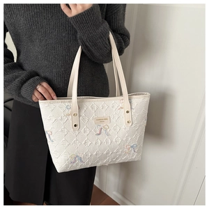 Detail of white quilted tote bag featuring floral ribbon embroidery and leather brand tag