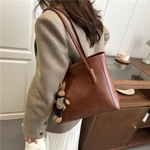 Brown vintage faux leather tote bag with a cute rabbit charm in a modern interior setting