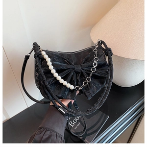 Detail of black pleated crossbody bag featuring a large bow and pearl accent chains