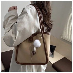 Vue latérale du sac fourre-tout beige minimaliste avec bordure marron et pompon blanc