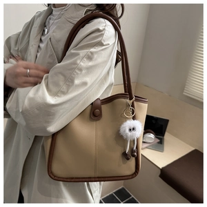 Detail of beige underarm bag with brown trim and cute plush monster pendant accessory
