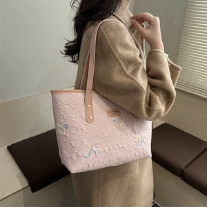 Pink tote bag with sequin bows and embossed texture, worn as a stylish shoulder bag