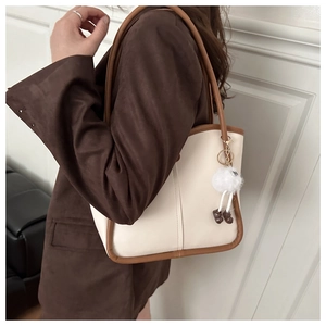 Detail of cream white tote bag with deep brown leather trim and fluffy pompom charm