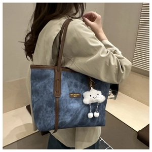 Detail of blue denim tote bag with brown leather handles and cloud plush charm