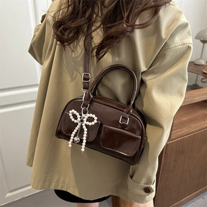 Deep brown glossy crossbody bag with double front pockets and pearl bow charm detail