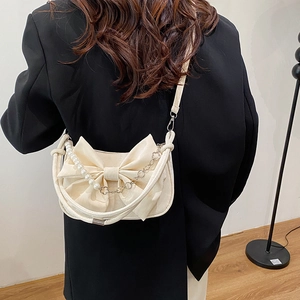 Chic cream crossbody bag featuring a large bow and pearl chain, worn on a black blazer
