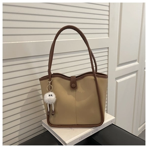 Detail of minimalist beige tote bag with brown trim and cute plush eye charm on strap