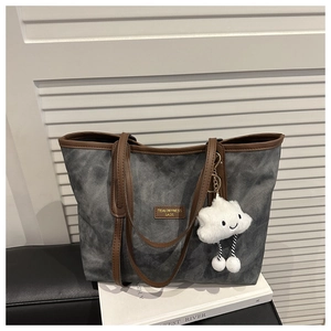 Detail of grey textured tote bag with brown leather straps and a plush cloud charm