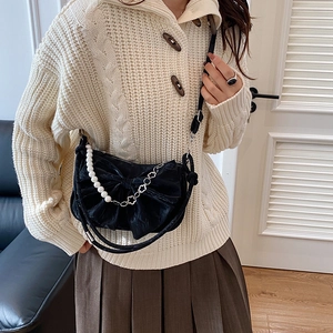 Chic black bow shoulder bag with pearl strap and metal chain shown on model in a cozy room
