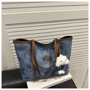 Detail of washed denim tote with brown leather straps and a plush cloud accessory
