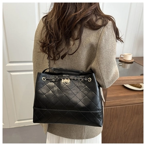 Detail of black quilted shoulder bag with gold chain strap worn by a model