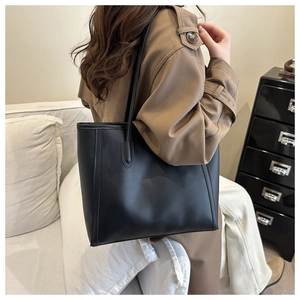 Detail of minimalist black matte leather tote bag worn by a model in a camel coat