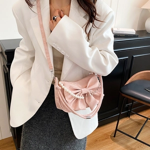 Chic pink crossbody bag with a large bow and pearl chain, styled on a white blazer