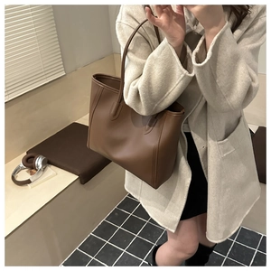 Deep brown leather tote bag paired with a beige wool coat in a lifestyle indoor setting