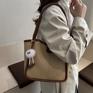 Minimalist beige underarm bag with dark brown edges and a cute plush monster pendant