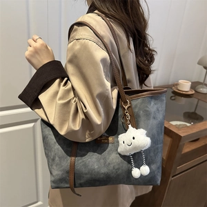 Gray textured tote bag with brown leather straps and cloud charm in a cozy indoor setting