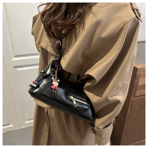 Detail of a black geometric triangle shoulder bag with high-shine finish and charms