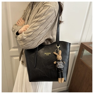 Detail of black leather tote bag with a golden logo and cute rabbit charm on a model