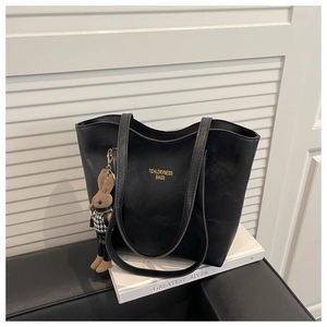 Detail of black PU leather tote bag featuring golden logo and plaid rabbit doll charm