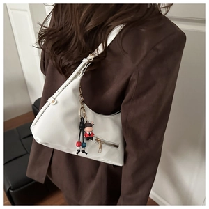 Close-up of a white crescent shoulder bag with bull charm and tassel on a model