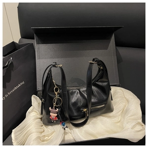 Close-up of black PU leather dumpling bag with metal zipper and cute cartoon cow pendant