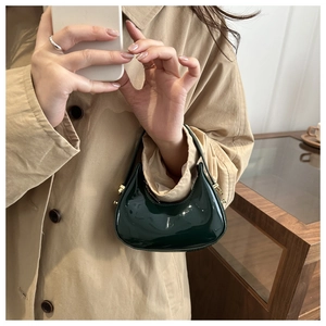 Detail of dark green patent leather handbag with gold buckle and glossy finish
