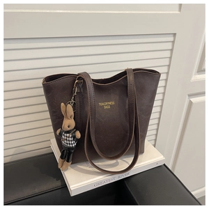Close-up of vintage brown pebble leather tote bag with a stylish rabbit charm on books