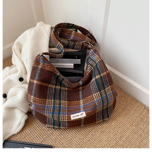 Macro shot of brown plaid hobo bag with text label on a soft knit sweater and carpet