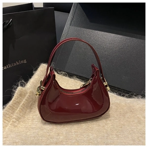 Close-up of a burgundy patent leather crescent bag with elegant gold hardware