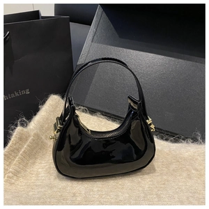 Detail of glossy black patent leather hobo bag with gold hardware on soft plush fabric