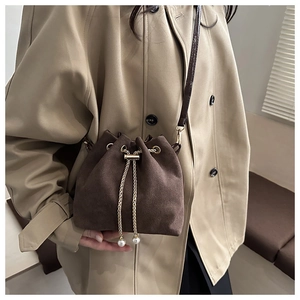 Detail of dark brown suede bucket bag featuring gold chain drawstring and pearl accents