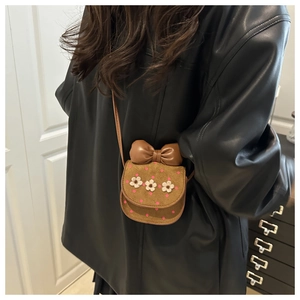 Brown crossbody bag detail featuring leather bow and white woven flower accents