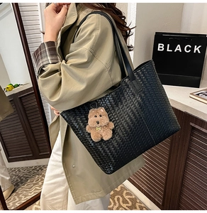 Detail of black woven tote bag with checkerboard texture and cute brown bear charm