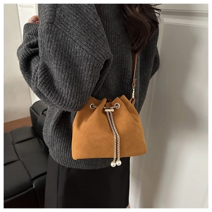 Brown frosted suede bucket bag with gold chain and pearl charm on a model's shoulder