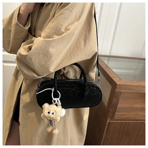 Detail of black leopard print pillow bag with a plush monster charm on a khaki trench coat