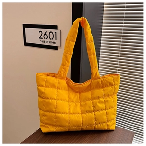 Detail of yellow quilted puffer tote bag with large square stitching on a wooden surface