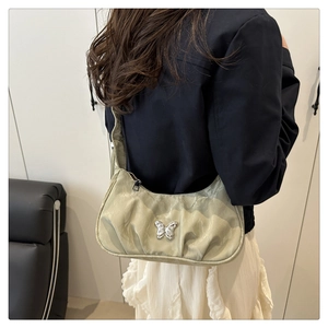 Detailed view of light green pleated shoulder bag with silver butterfly charm on model