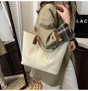 Detail of cream woven tote bag with dark brown leather straps and visible stitching