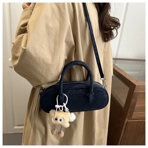 Deep blue suede cylinder pillow bag with cute plush charm on a model in trench coat