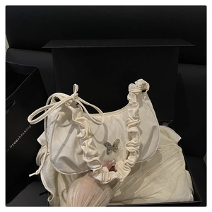 Detail of a beige pleated crossbody bag with a butterfly metal pendant and fine textures