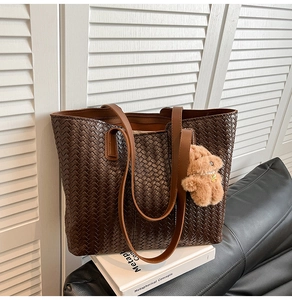 Detail of dark brown woven tote bag featuring soft leather texture and plush bear charm