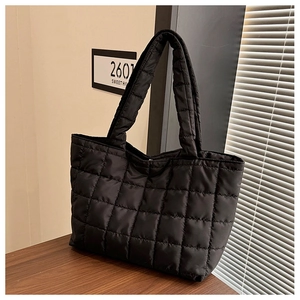 Detail of a black quilted tote bag with padded handles on a wooden table setup