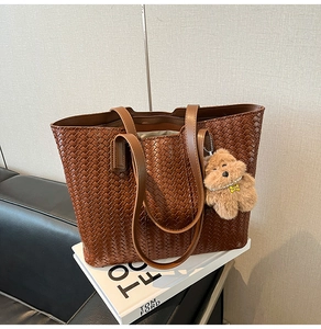 Close-up of brown woven leather tote bag with a cute plush puppy charm accessory
