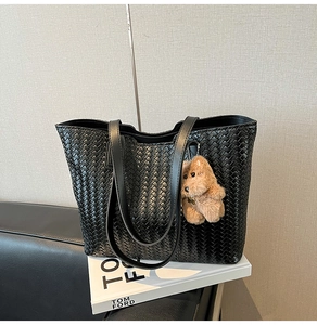 Close-up of black woven tote bag texture with a cute plush bear charm accessory