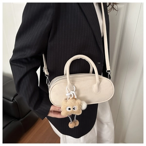 Chic beige leather pillow bag with brown plush monster charm on model in striped blazer