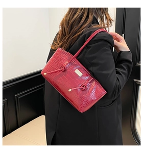 Détail d'un sac bandoulière rouge effet crocodile avec logo métallique et lanière
