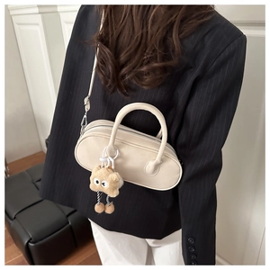 Detail of a creamy white pillow bag styled with a tailored suit and plush charm accessory