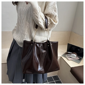Detail view of large brown tote bag showing golden chain strap and textured faux leather
