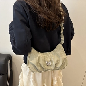 Light green pleated underarm bag with silver butterfly buckle shown on model in black jacket